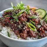 Steaming bowls of Easy Korean Beef Bowl, topped with crisp cucumber, julienned carrot, and sesame seeds over fluffy rice.  