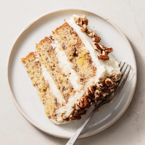 Golden-brown layers of Hummingbird Cake filled with cream cheese frosting and toasted pecan garnish.