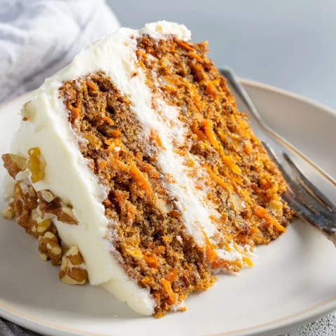 A close-up of frosted carrot cake slices revealing moist crumb and chopped nuts.