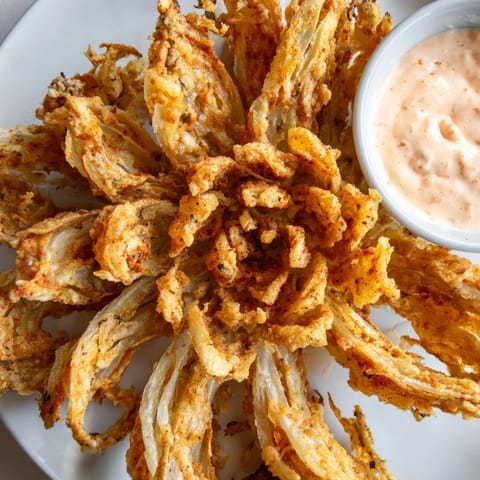 A close-up of Onion Petals on a rustic platter, their crunchy coating glistening, paired with a creamy reddish dip perfect for sharing as an appetizer.