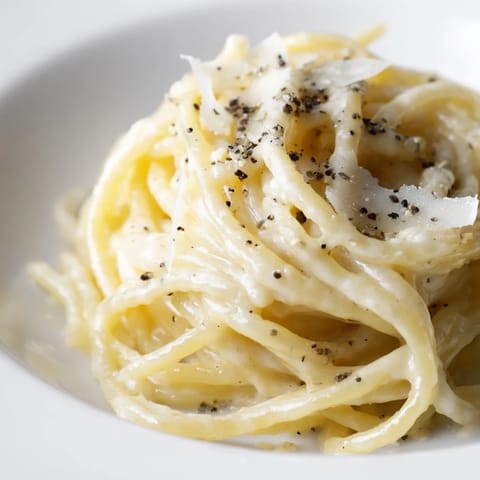 Glossy spaghetti cacio e pepe is twirled on a fork, highlighting the velvety cheese sauce clinging to each al dente strand.
