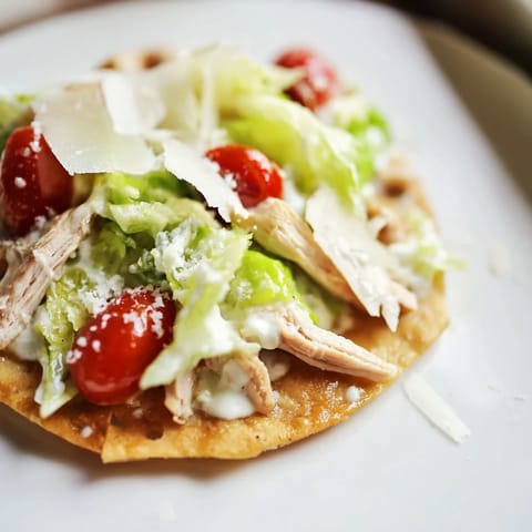 A close-up of Caesar Chicken Flatbread featuring crisp lettuce, shaved Parmesan, and bright cherry tomatoes on warm naan.