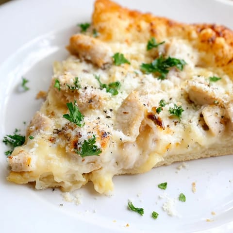 A close-up view of a golden, crispy Chicken Alfredo Pizza slice, revealing layers of melted mozzarella and tender chicken atop creamy Alfredo sauce.