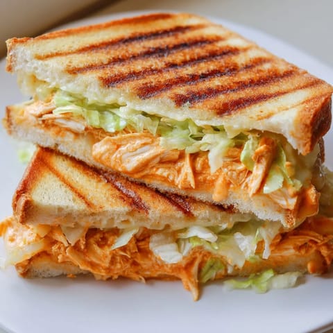 Golden Buffalo Chicken Caesar Grilled Cheese slices on a plate, showcasing melted provolone and fresh romaine between crispy sourdough.