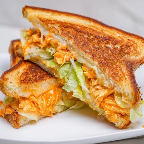A close-up of a Buffalo Chicken Caesar Grilled Cheese, featuring gooey cheese and a drizzle of spicy buffalo sauce.