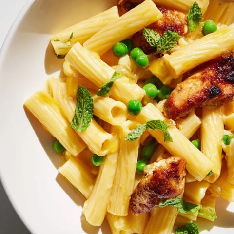Fork-twirled penne in a glossy lemon sauce with tender chicken, sweet peas, and fresh mint leaves for a bright spring dinner.