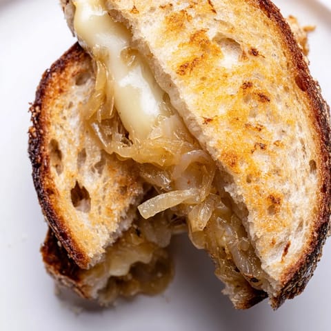 Golden-brown Caramelized Onion & Gruyère Grilled Cheese oozing melted cheese on rustic bread.