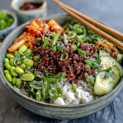 A bowl of Korean Ground Beef Bowl features gochujang-spiced meat, colorful veggies, and sesame seeds over fluffy rice.  