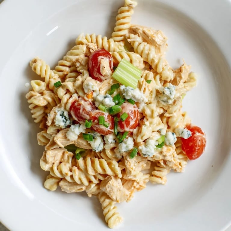 Colorful bowl of Buffalo Chicken Pasta Salad with juicy cherry tomatoes, crisp onions, and herbs, ready for a potluck.
