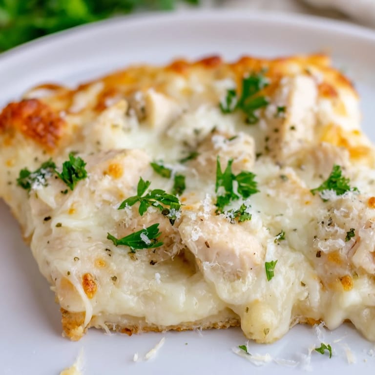 Sliced Chicken Alfredo Pizza rests on a wooden board, showcasing its bubbly cheese crust and garnished with fresh parsley for color.