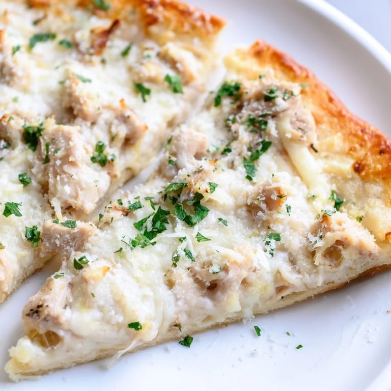 Homemade Chicken Alfredo Pizza on a baking sheet, featuring a golden edge, generous cheese topping, and succulent pieces of chicken.