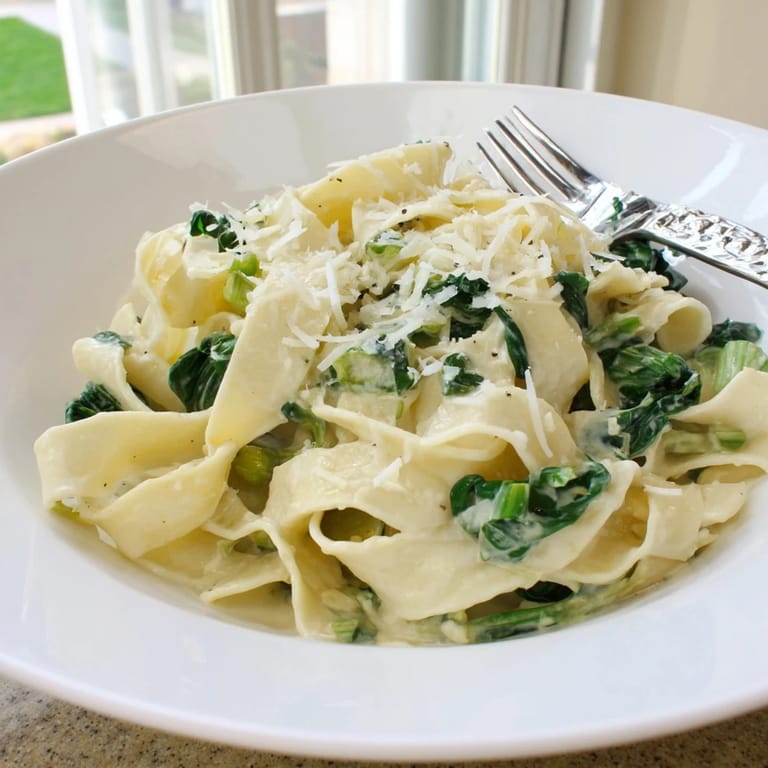 Tossing cooked egg noodles in a rich, garlicky cream sauce with wilted spinach in a stainless steel skillet.
