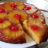 Freshly baked Pineapple Upside-Down Cake featuring golden, caramelized pineapple rings and bright red cherries on a moist vanilla base.