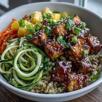 Crispy baked tofu and colorful spiralized veggies atop fluffy quinoa in an Easy Teriyaki Quinoa Bowl.